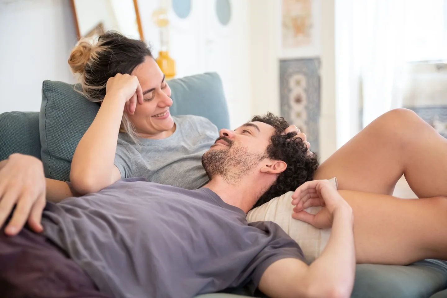 Un couple adulte se détend sur un canapé, l'homme pose sa tête sur les genoux de la femme qui sourit